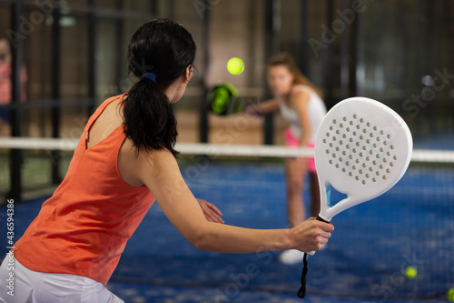 Obraz na plátně Rear view of brunette girl with white racket playing padel tennis at court