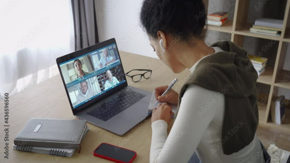 Happy African American mixed race adult student having virtual meeting with diverse people online call elearning webinar at home office talking writing notes. Video e learning conference call on pc.
