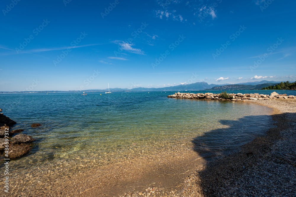 Beautiful beach on Lake Garda (Lago di Garda) in front of the small village of Lazise. Verona province, Veneto, Italy, southern Europe. Lombardy coast on the horizon with mountains and hills.