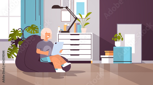 schoolgirl using tablet pc happy girl sitting on beanbag and doing homework education concept living room interior