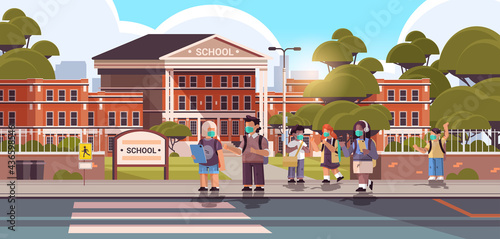 schoolchildren wearing masks to prevent coronavirus pandemic pupils standing together near school building