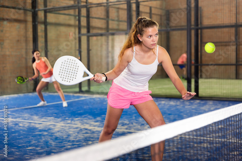 Portrait of sporty young brown-haired girl playing padel on indoor court, ready to hit ball. Healthy and active lifestyle concept. © JackF