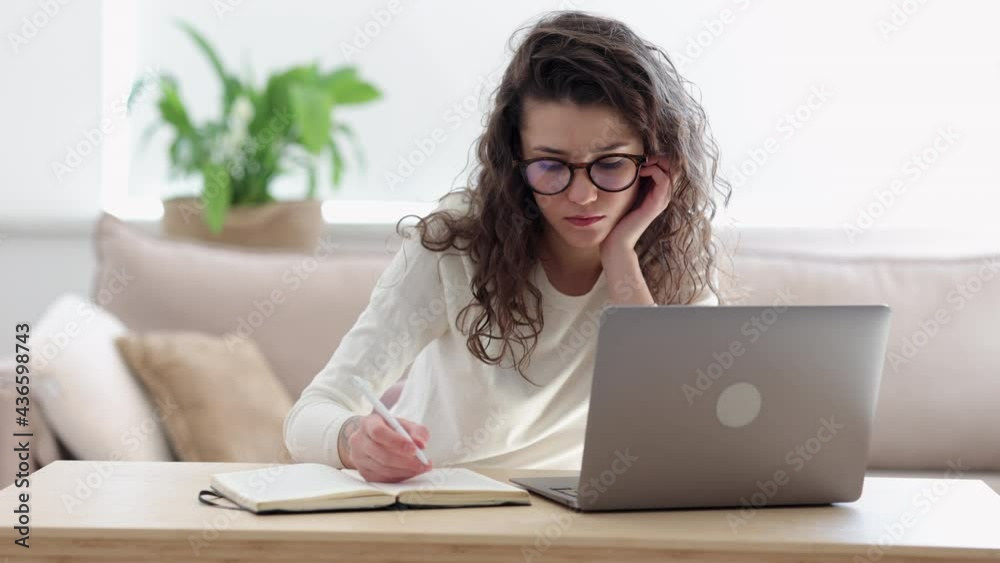 Woman student write note in notepad while researching for information on laptop Spbi. Freelancer