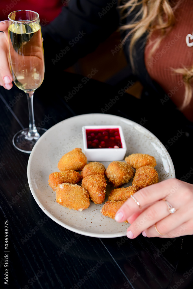 Deep fried mozarella cheese balls served on a white plate with sauce. Caucasian woman sitting in restaurant