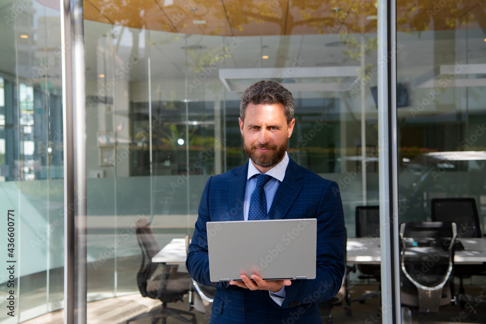 Business man holding laptop standing on the street near business office building. Business man holding laptop standing on the street near business office building.