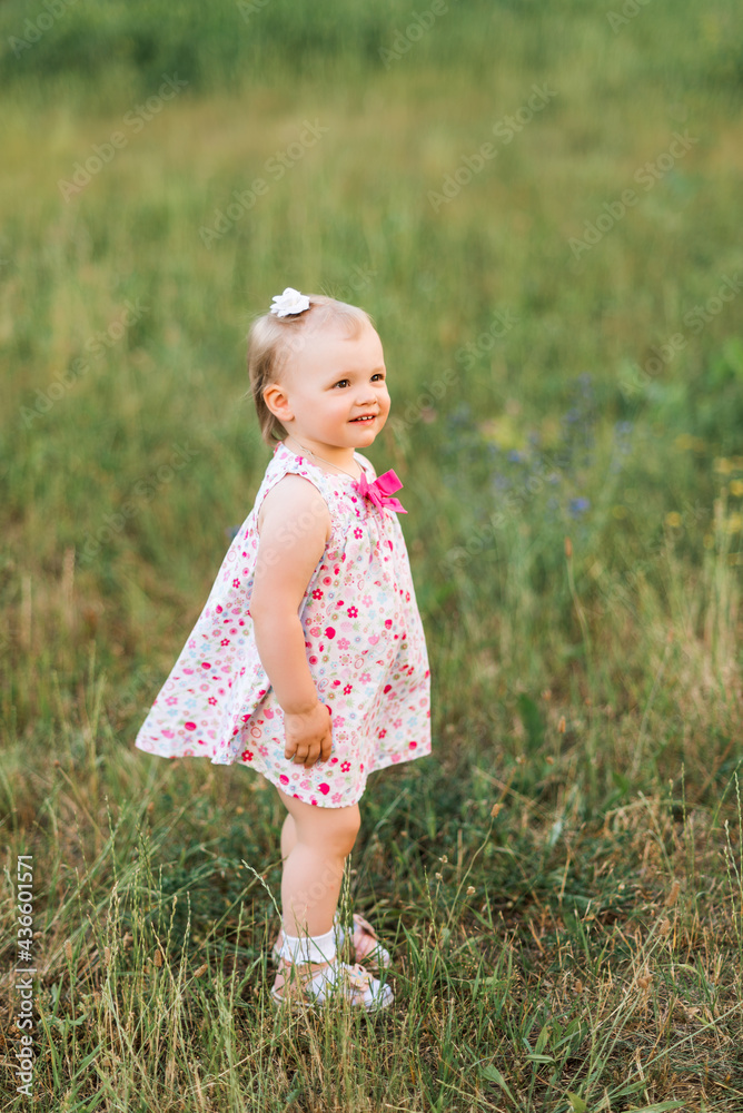 baby is standing in the grass. Summer photo with a little girl. A child walks in the park.