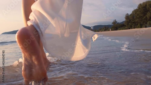 4K Slow motion woman feet walking barefoot on the beach at golden sunset time. leaving footprints in sand. Female tourist on summer vacation holiday relax at tropical beach Phuket, Thailand.