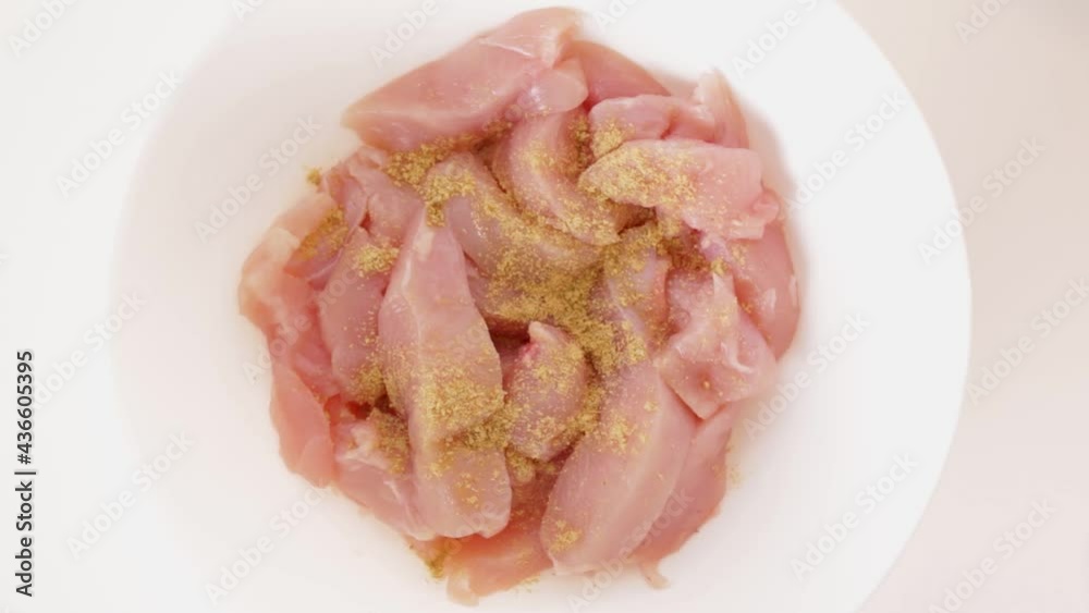 Pouring different spices and milk on raw chicken breast, close up Pouring different spices and milk on raw chicken breast, close up