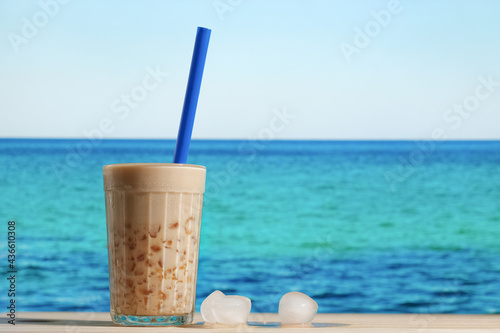 Glass of cold bubble tea and ice cubes. Summer resort, beach bar concept. Milk boba tea with tapioca pearls, blue sea on background. 