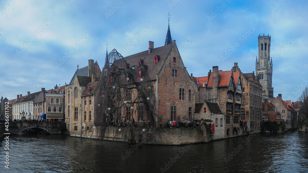 Bruges cityscape. The old, medieval houses are placed near a canal. The bell tower can be seen in background. Belgium