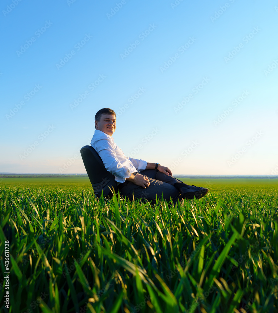 businessman sits in an office chair in a field and rests, freelance and business concept, green grass and blue sky as background