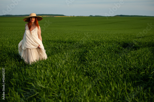 Pregnant woman on the summer green field wearing long white dress