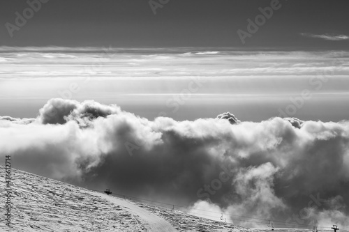Snowy ski slope and beautiful sky with clouds at evening. Black and white toned landscape.