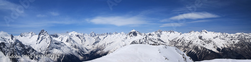 Panorama of high snow-capped mountain peaks and beautiful blue sky with clouds at sunny day