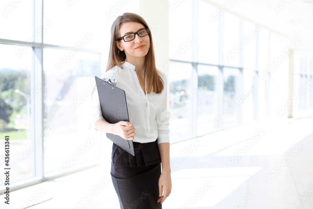 Beautiful female specialist with clipboard standing in modern office and smiling charmingly. Working on design, data analysis, plan strategy. Business people concept Beautiful female specialist with clipboard standing in modern office and smiling charmingly. Working on design, data analysis, plan strategy. Business people concept