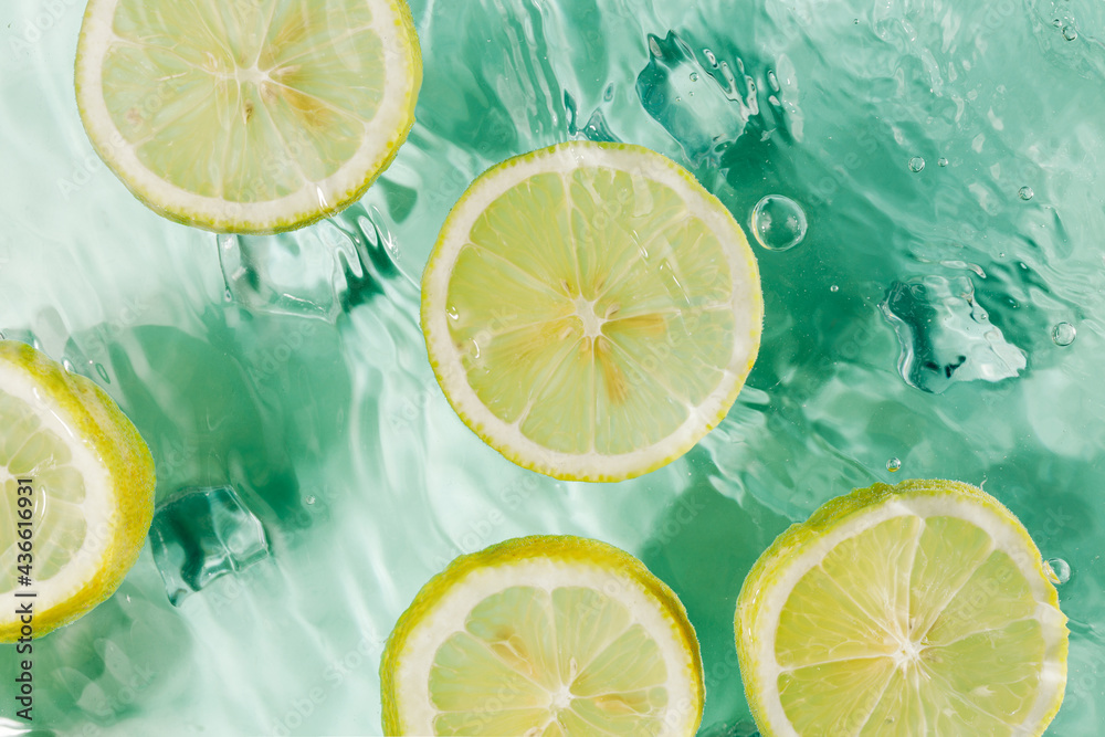 Summer scene with round slices of lemons floating in the turquoise water. Creative food or drink concept. Refreshing drink with ice cubes and fruit in splash of water. Flat lay, top view. Summer scene with round slices of lemons floating in the turquoise water. Creative food or drink concept. Refreshing drink with ice cubes and fruit in splash of water. Flat lay, top view.
