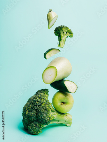 Cut broccoli and zucchini with green apple isolated on a light blue background. Fresh and healthy ingredients for a vegan diet. Salad with veggies falling down. Creative food concept.