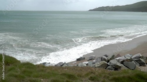 Windy overcast day at UK Devon beach on the South West coastal path filmed in slow motion. Waves crashing onto pebble beach with start point lighthouse in the distance. photo