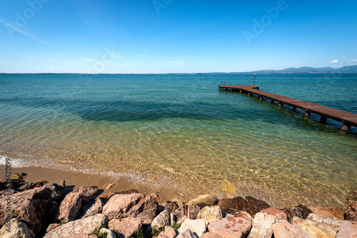 Beautiful beach with a small empty wooden pier on Lake Garda (Lago di Garda) between the small villages of Lazise, Bardolino and Cisano. Tourist resort in Verona province, Veneto, Italy, Europe. photo