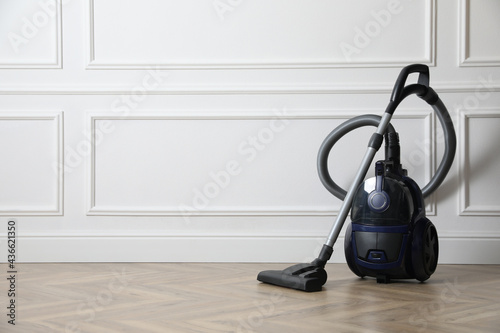 Modern vacuum cleaner near white wall indoors, space for text