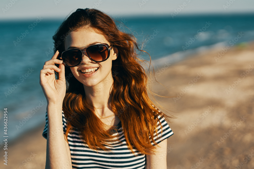 portrait of happy red-haired woman in nature on the beach near the sea and glasses on her face portrait of happy red-haired woman in nature on the beach near the sea and glasses on her face