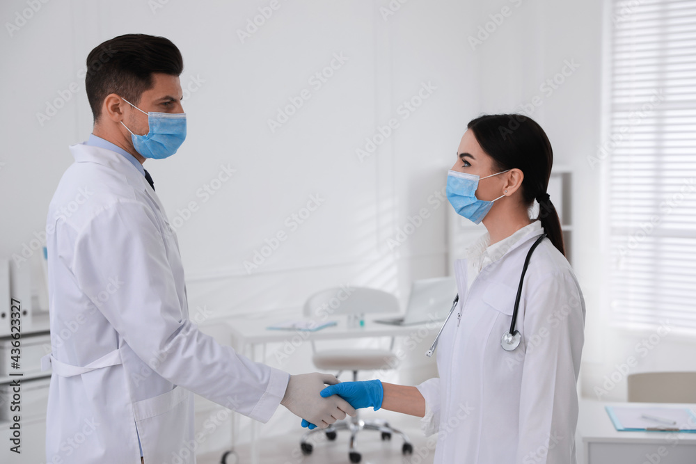 Doctors in medical gloves with protective masks giving handshake at hospital Doctors in medical gloves with protective masks giving handshake at hospital