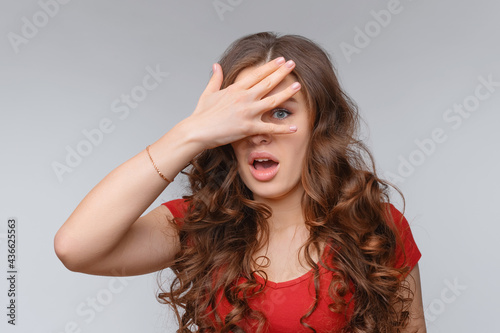 Portrait of scared and anxious young brunette woman, covering eyes with hand, peeking through fingers worried, panicking