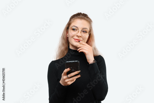 Image of a thoughtful young beautiful woman in casual clothes holding her smart phone. White background