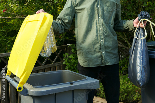 Person performing a selective sorting of household waste in recycling bins. Man putting plastic bottles in a yellow container and garbage in a bag in a green container.	