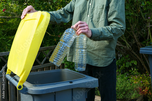 One person making a selective sorting of waste. Man putting plastic bottles in a yellow bin for recycling.	 photo