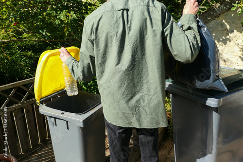 Person performing a selective sorting of household waste in recycling bins. Man putting plastic bottles in a yellow container and garbage in a bag in a green container.	