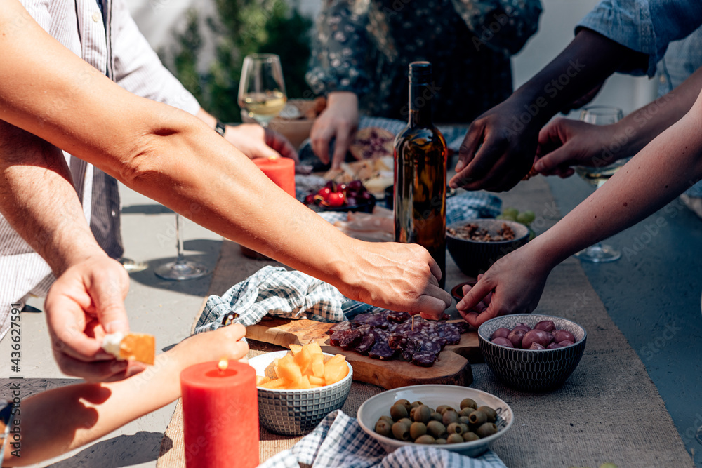 people outdoor picking up food appetizer tapas from a long table with a glass bottle of wine in the middle. summer party family gathering.