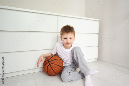 Portret of a little smiling schoolboy looking at camera sitting on the floor at his white room
