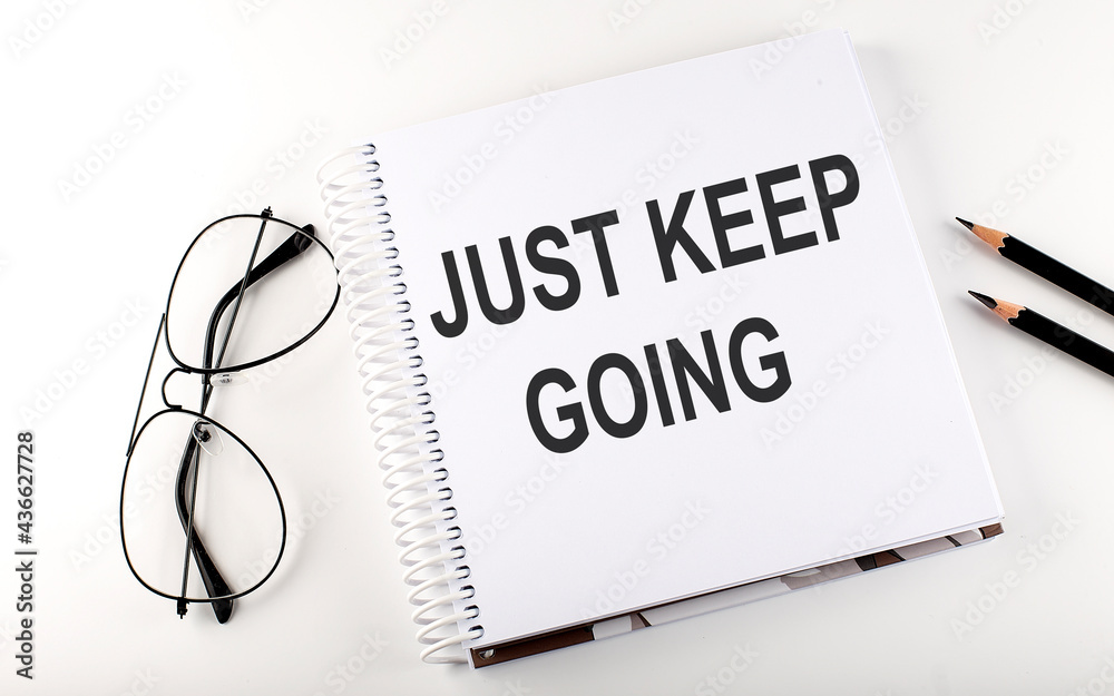 Notebook with text JUST KEEP GOING on the white background Notebook with text JUST KEEP GOING on the white background