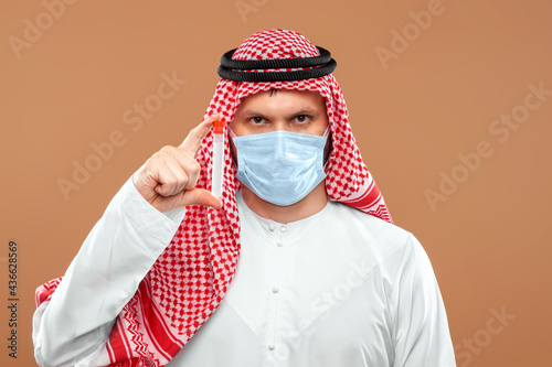 A masked Arab man holds a test tube in a national costume on a beige background. photo