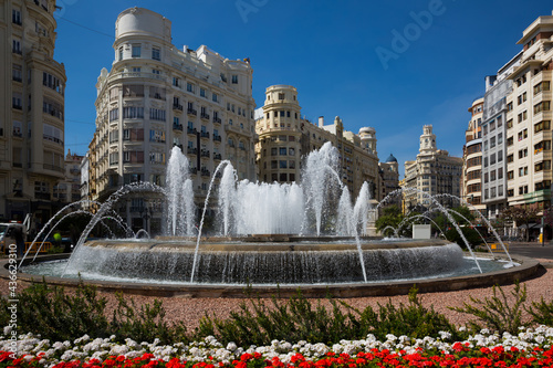 Picturesque spring cityscape of central square of Valencia with impressive round fountain surrounded with flowers, Spain
