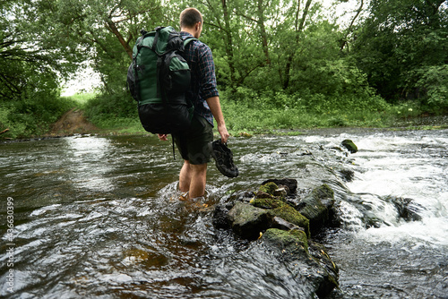 Fotografie Low section shot of a man in a plaid shirt with heavy hiking backpack crossing t