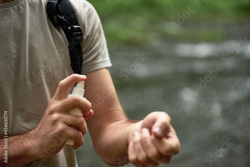 Male tourist using mosquito and tick repellent spray outdoors during hiking