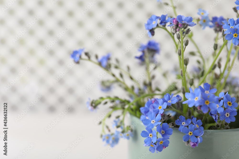 Fototapeta premium Beautiful blue forget-me-not flowers in cup against blurred background, closeup. Space for text