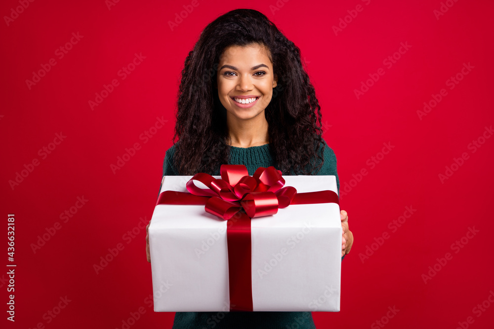 Photo of lucky excited dark skin woman dressed green pullover smiling holding big gift isolated red color background Photo of lucky excited dark skin woman dressed green pullover smiling holding big gift isolated red color background