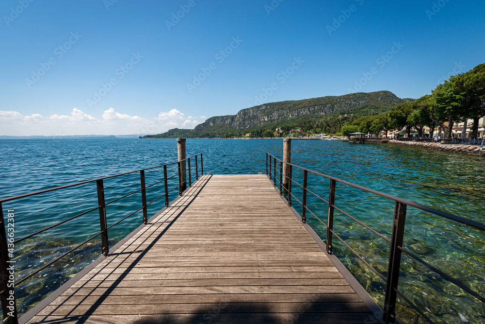 Wooden pier on Lake Garda (Lago di Garda) in front of the small town of Garda, bay with the Headland of San Vigilio (Punta San Vigilio). Tourist resort in Verona province, Veneto, Italy, Europe.