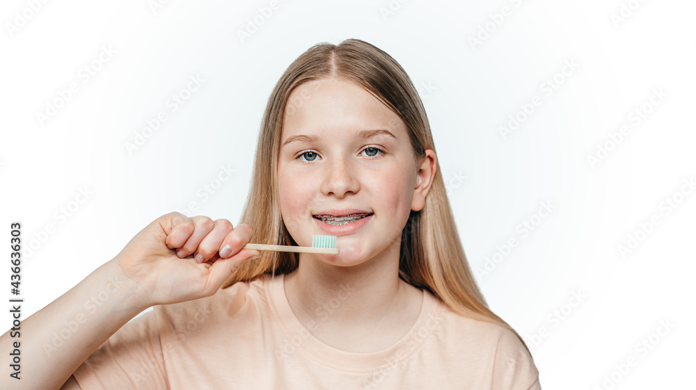 Smiling blonde girl with orthodontic braces holding holding an eco friendly bamboo toothbrush Smiling blonde girl with orthodontic braces holding holding an eco friendly bamboo toothbrush