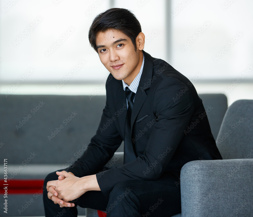 Portrait 20s handsome young successful Asian businessman wearing formal suit with necktie, smiling confidently and intelligently, sitting on comfortable sofa indoor office, posing, looking at camera. Portrait 20s handsome young successful Asian businessman wearing formal suit with necktie, smiling confidently and intelligently, sitting on comfortable sofa indoor office, posing, looking at camera.