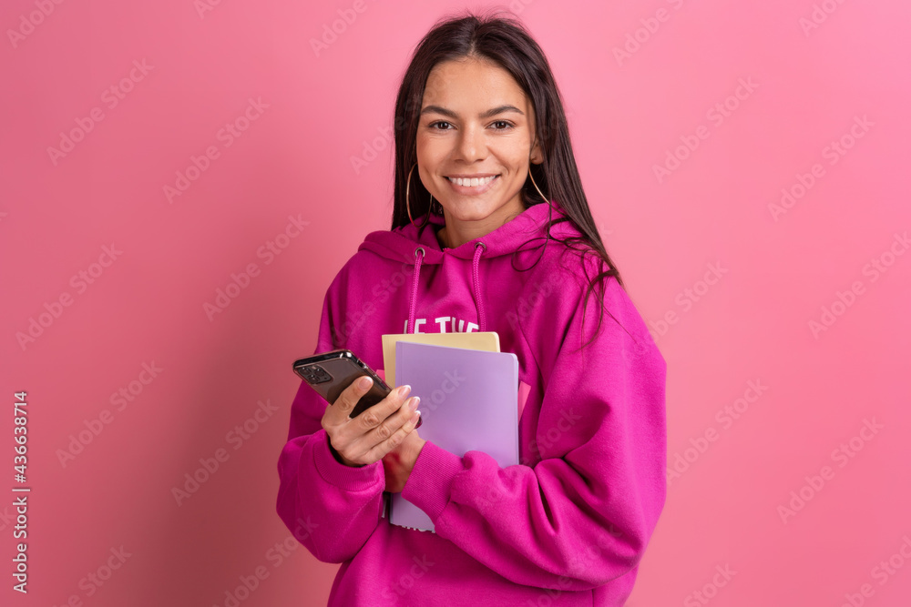 hispanic pretty woman in pink hoodie smiling holding holding notebooks and using smartphone hispanic pretty woman in pink hoodie smiling holding holding notebooks and using smartphone