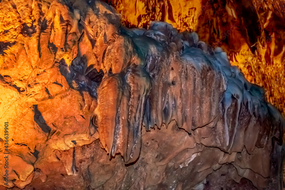 Naklejka premium Mineral formations on the walls of Damlatas cave in Alanya (Turkey), close-up. Abstract geological natural background in yellow-brown-blue colors