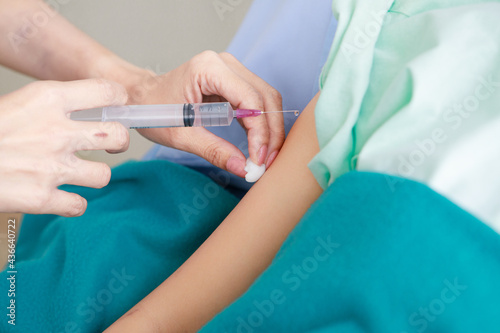 Asian young long hair female patient wears green hospital uniform covered by blanket lay down on blue pillow bed feel pain when doctor shot medicine injection by needle and syringe into right arm
