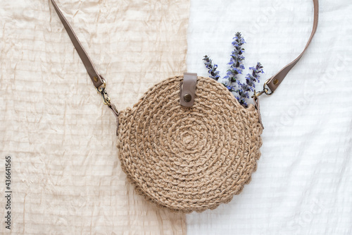 Beautiful handmade knitted round bag made of natural jute material on a white and beige fabric background.