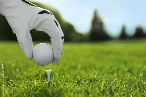 Golfer putting ball on tee at green course, closeup. Space for text