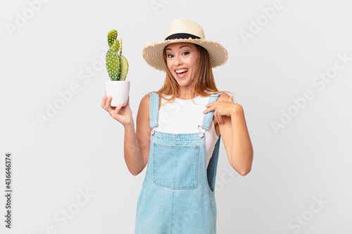 pretty woman feeling happy and pointing to self with an excited and holding a cactus decorative plant photo