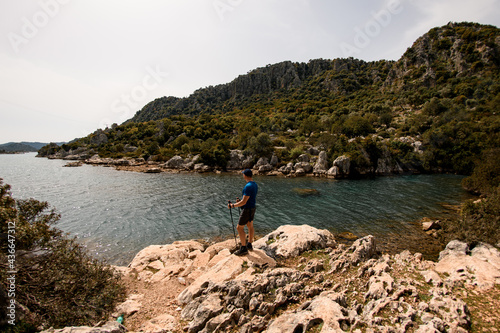 rear view of male tourist standing on stone and enjoying the sea and mountain scenery